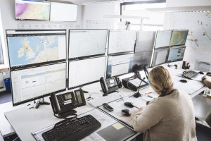Eine Frau sitzt vor einer Wand aus Monitoren in der 24/7 Betriebswarte für die Offshore und Onshore Windparks. Hier werden u.a. auch PV und BESS Systeme überwacht.